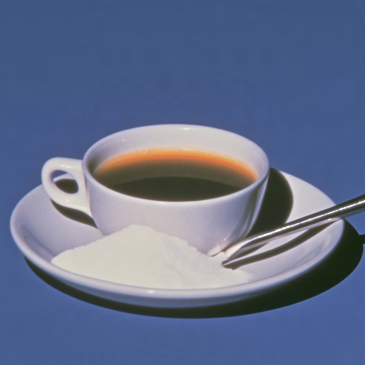 A cup of black coffee with white powder on the side on a blue background