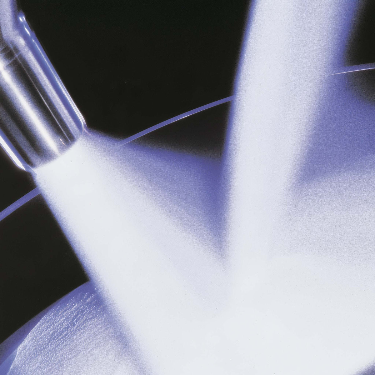 White powder coming out of a stainless steel nozzle and into a drum of bulk white powder.